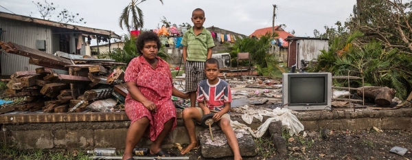 A woman and her children sitting on a brick wall of what used to be their home in Fiji. Their house was just a few meters from the shoreline and suffered extensive damage during strong storm surges at the height of Cyclone Winston.