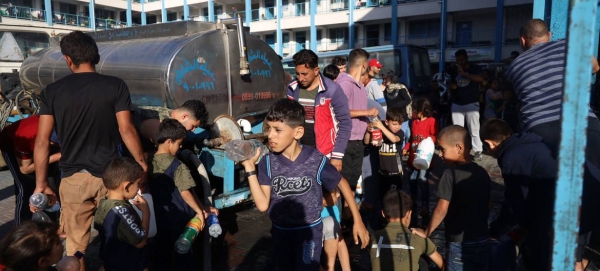 Children in Gaza gather at a water truck to fill bottles with clean drinking water.