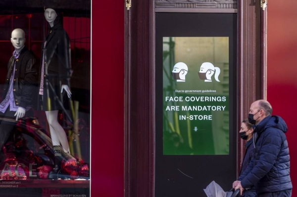 يمشي الناس أمام لافتة تطلب من الناس ارتداء أغطية الوجه في لندن.  (شينخوا)