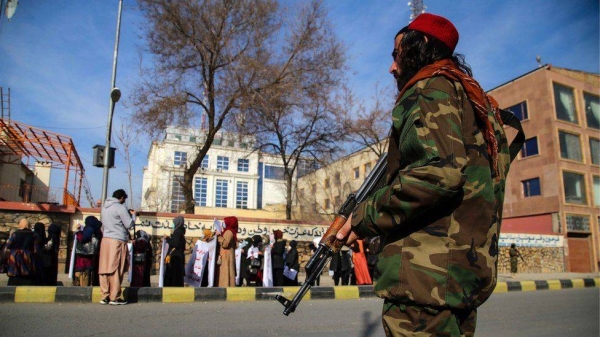 Taliban guard standing as women carry placards during a rally demanding the international community unfreeze the country's assets.