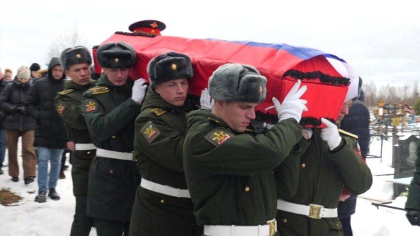 Russian servicemen carry a coffin draped in the national flag through a snowy cemetery.
