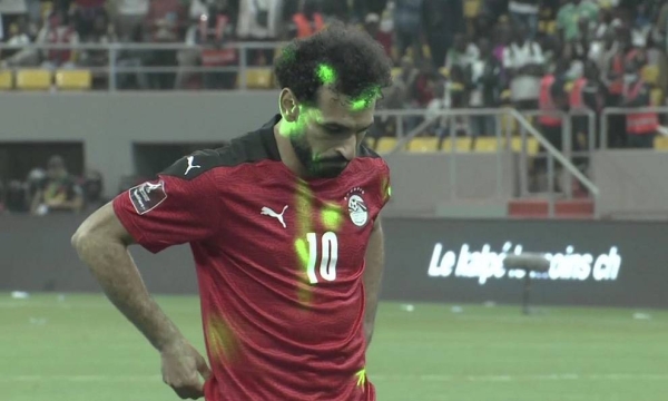 Mohamed Salah prepares to shoot a penalty while spectators point lasers at him.