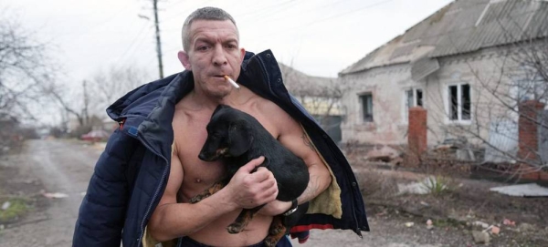 A man holds a dog as he walks past a damaged house following shelling in Mariupol, in southeastern Ukraine. — courtesy UNICEF/Evgeniy Maloletka