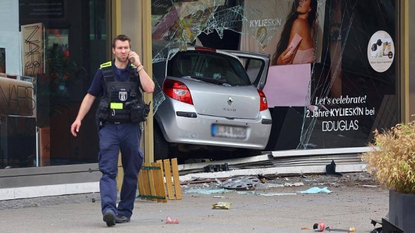 A police officer speaks on the phone near the car at crashed into a group of people and ended up in a storefront.
