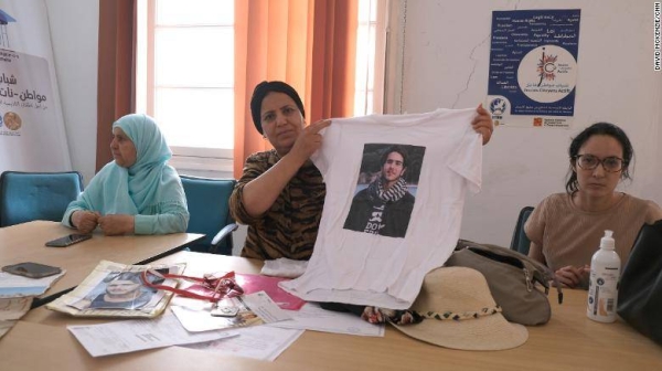 Samia stands by a mural of her son in their hometown of Kelibia. She said his friends, who regularly visit her, painted it. The drawing has his face, the date of his disappearance, a map of Tunisia and says 