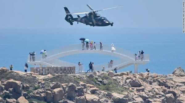 Tourists look on as a Chinese military helicopter flies past Pingtan island, one of mainland China's closest point from Taiwan on August 4, 2022.