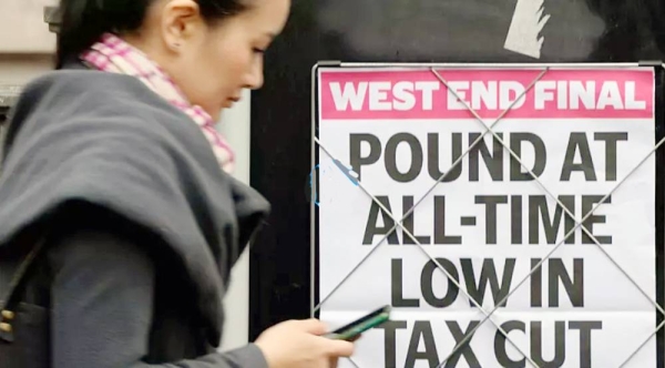 A woman walks past a headline in London announcing a record low value of the pound, Tuesday, Sept. 27, 2022.