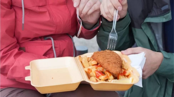 A couple eating fish and chips using a plastic fork from a single-use tray.