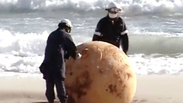 Two police officers examine the big metal boulder found on the beach in Hamamatsu. — courtesy NHK