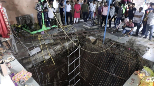 People stand around the collapsed flooring where people fell into a well at a temple in Indore, India, on March 30
