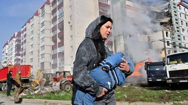 A woman, carrying a child, walks passed a damaged appartment building in Uman.