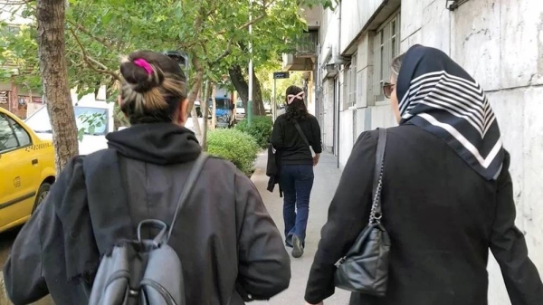 Two women walking down a street, facing away from the camera — one is wearing a headscarf and one is not. — courtesy handout photo