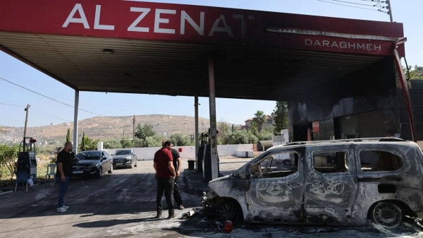 People stand near a burnt car, reportedly set ablaze by Israeli settlers, at a gas station in Al-Lubban Al-Gharbi in the occupied West Bank on June 21, 2023.