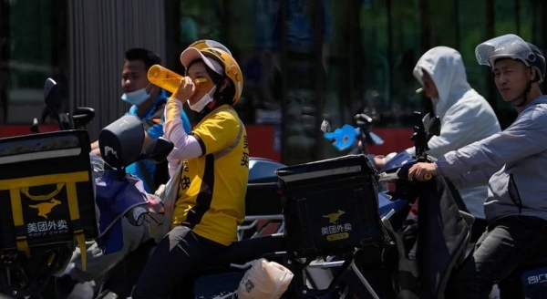 A delivery rider drinks water as she and other motorists wait to cross a street on a hot day in Beijing, Wednesday, June 21, 2023.