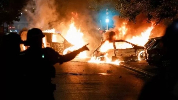 Police officers stand near burning cars during protests in Nanterre, west of Paris