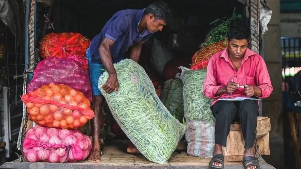 A laborer carries a sack of green beans at a market in Colombo.