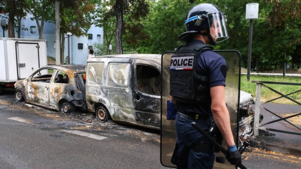 A French police officer stands guard next to vehicles burnt during a night of clashes between protesters and police, in Nanterre, Paris, on July 1, 2023.