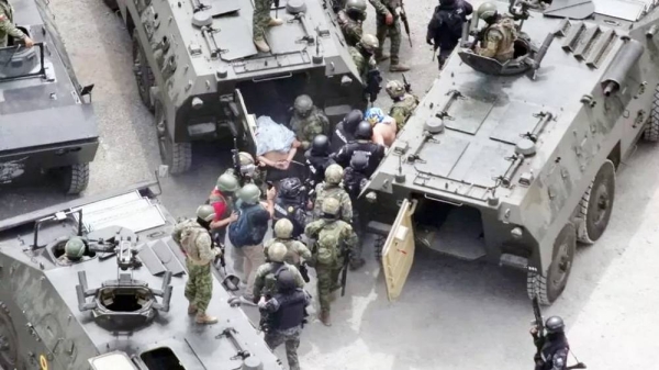 Two handcuffed men with shirts over their heads are moved into tanks by Ecuador police. — courtesy Reuters