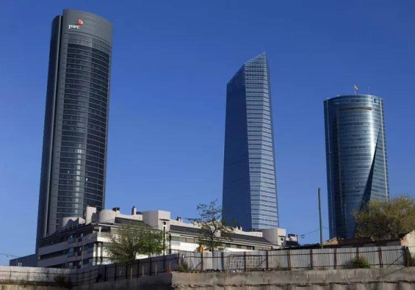 A man looks over a fence in front of office towers in the business district of Madrid, Spain