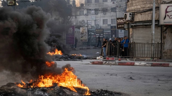 Palestinian youths take cover behind a wall during confrontations with Israeli forces in the occupied West Bank city of Jenin on November 9, 2023