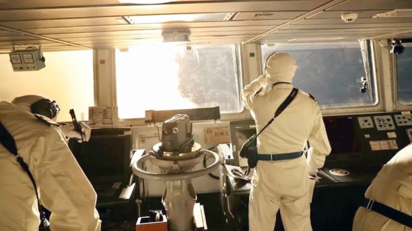 Two figures stand in a room of the HMS Diamond, looking out at a fiery scene. — courtesy UK Ministry of Defense.