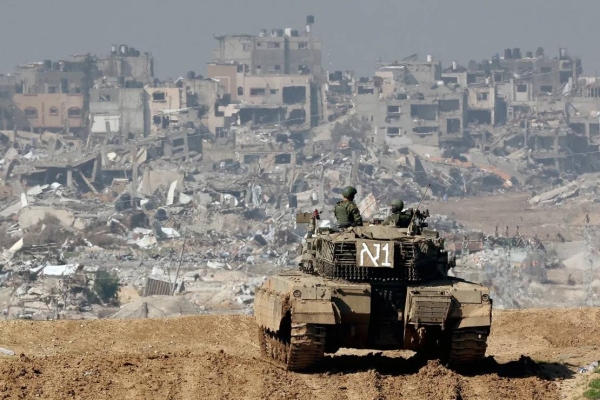 An Israeli tank along a fence on January 19, 2024, as damaged buildings are seen in the Gaza strip amid continuing battles between Israel and Hamas