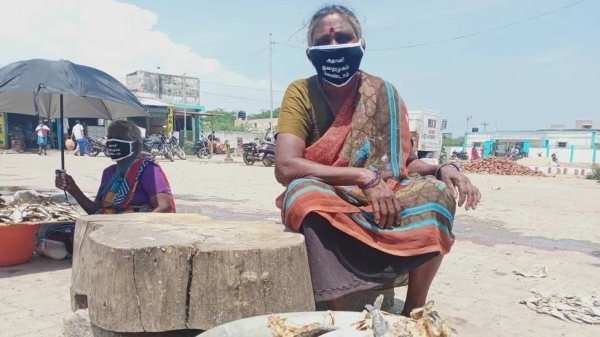 Protesters wearing masks which say, 'We don't need an Adani Port', sit in a village market in Tamil Nadu