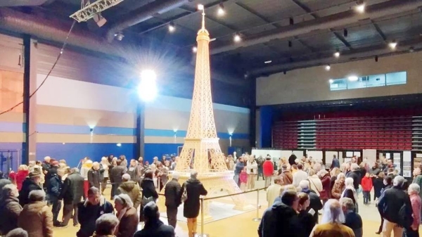 Tall Eiffel Tower made out of matchsticks in the middle of a room full of people. — courtesy Richard Plaud/Reuters