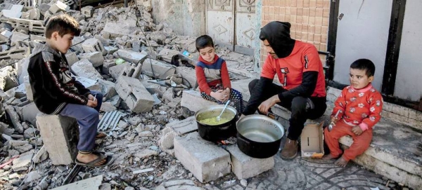 A man cooks food for his children over a wood fire in front of his destroyed home in an area west of Gaza City. — courtesy UNICEF/Omar Al-Qattaa