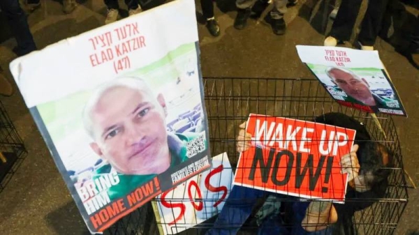 A man sits in a cage with portraits of hostage Elad Katzir during a demonstration in Tel Aviv in March. — courtesy AFP