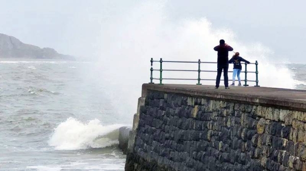Two people watch the stormy seas at the end of a pier in Criccieth, Wales. — courtesy BBC Weather Watcher/snaphappydave