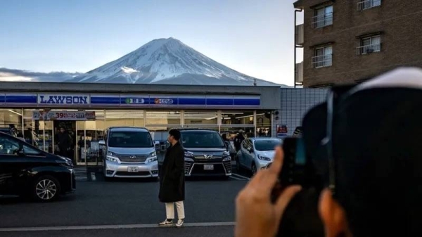 
An image showing a photo being taken of a person standing in front of a Lawson shop, with Mount Fuji in the background. — courtesy Getty Images