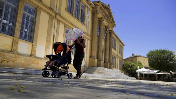 A woman protects herself from the sun with an umbrella as she push a baby in a pushchair during a hot day at Phaneromeni square in central capital Nicosia