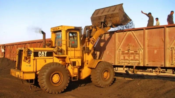 A yellow CAT digger loads coal onto a train in Pakistan