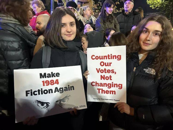 Demonstrators look at a photographer as they hold posters during an opposition protest against the results of the parliamentary election in Tbilisi, Georgia, October 28, 2024