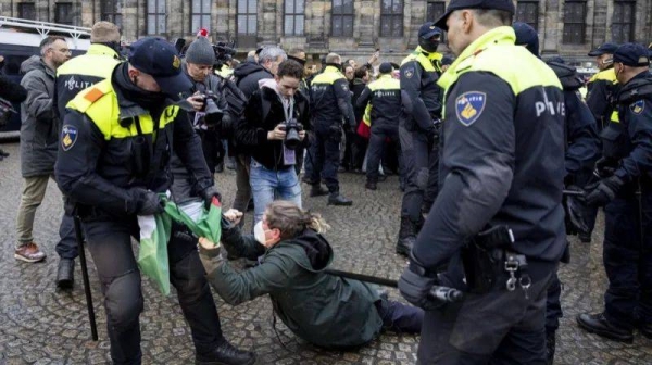 Dutch police detain a pro-Palestinian protester in Dam Square. The protester is wearing a face mask and lying on the ground while the policeman tries to take a Palestinian flag off her
