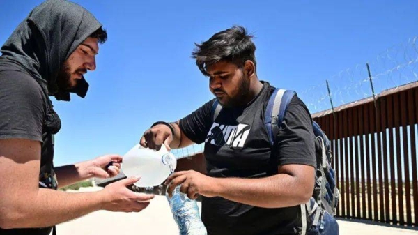 Migrants from India share water in the intense heat after walking into the US from Mexico in June