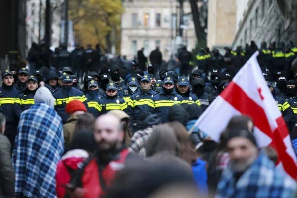 Protesters with a Georgian national flag stand in front of police blocking the entrance of the Parliament's building in Tbilisi, Georgia, Monday, Nov. 25, 2024