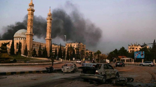 Smoke billows in the distance as damaged cars are seen at the site of Syrian regime airstrikes targeting opposition fighters in Aleppo, in northern Syria, on November 30, 2024