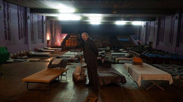 A man waits for evacuation to western Ukraine as he stands by a bed in a city theatre that hosts refugees running from Russian offensive in the Donetsk region, in Pavlohrad