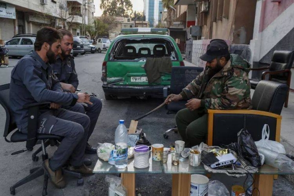 Syrian fighters sit in a street as they guard a police station in Damascus, Syria, Tuesday, Dec. 17, 2024