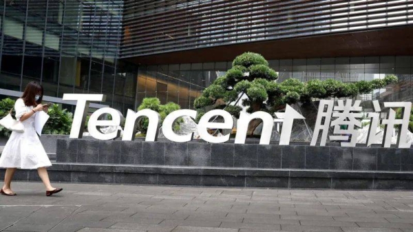 A woman in a white dress, looking at her phone and wearing a face mask, walks outside the headquarters of Tencent in Shenzhen, China