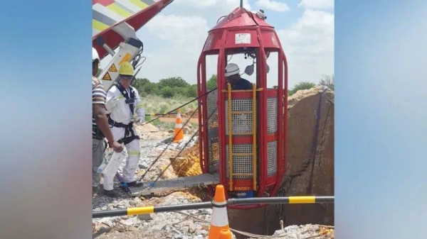 A cage is being lowered down from the top of the disused shaft to bring the miners back to the surface