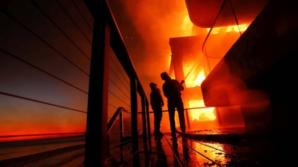 Firefighters work from a deck as the Palisades Fire burns a beachfront property in Malibu on Wednesday