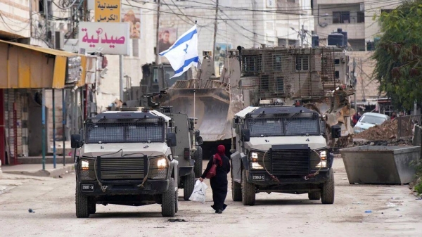 A Palestinian woman walks past Israeli army vehicles during a military raid in Jenin in the occupied West Bank, on Wednesday