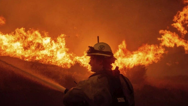 A firefighters spray water as he monitor flames caused by the Hughes Fire along a roadside in Castaic, Calif., Wednesday, Jan. 22, 2025