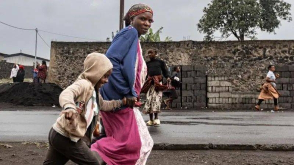 A woman in a pink dress and blue top and child run on a street in Goma