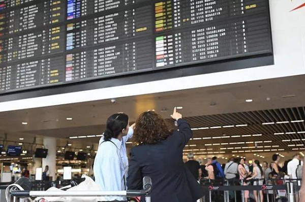 Travelers wait for information in front of a departure board at Brussels International Airport in Brussels, 19 July, 2024