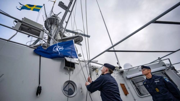 Captain Thomas Zimmerman, right, gives the order to hoist the NATO flag on the patrol ship HMS Carlskrona (P04) set sail from the naval port in Karlskrona, Sweden