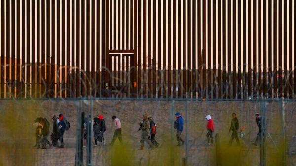 Migrants seeking asylum in the United States gather near the border wall after crossing a razor wire fence as a member of the Texas National Guard escorts them on December 19, 2024